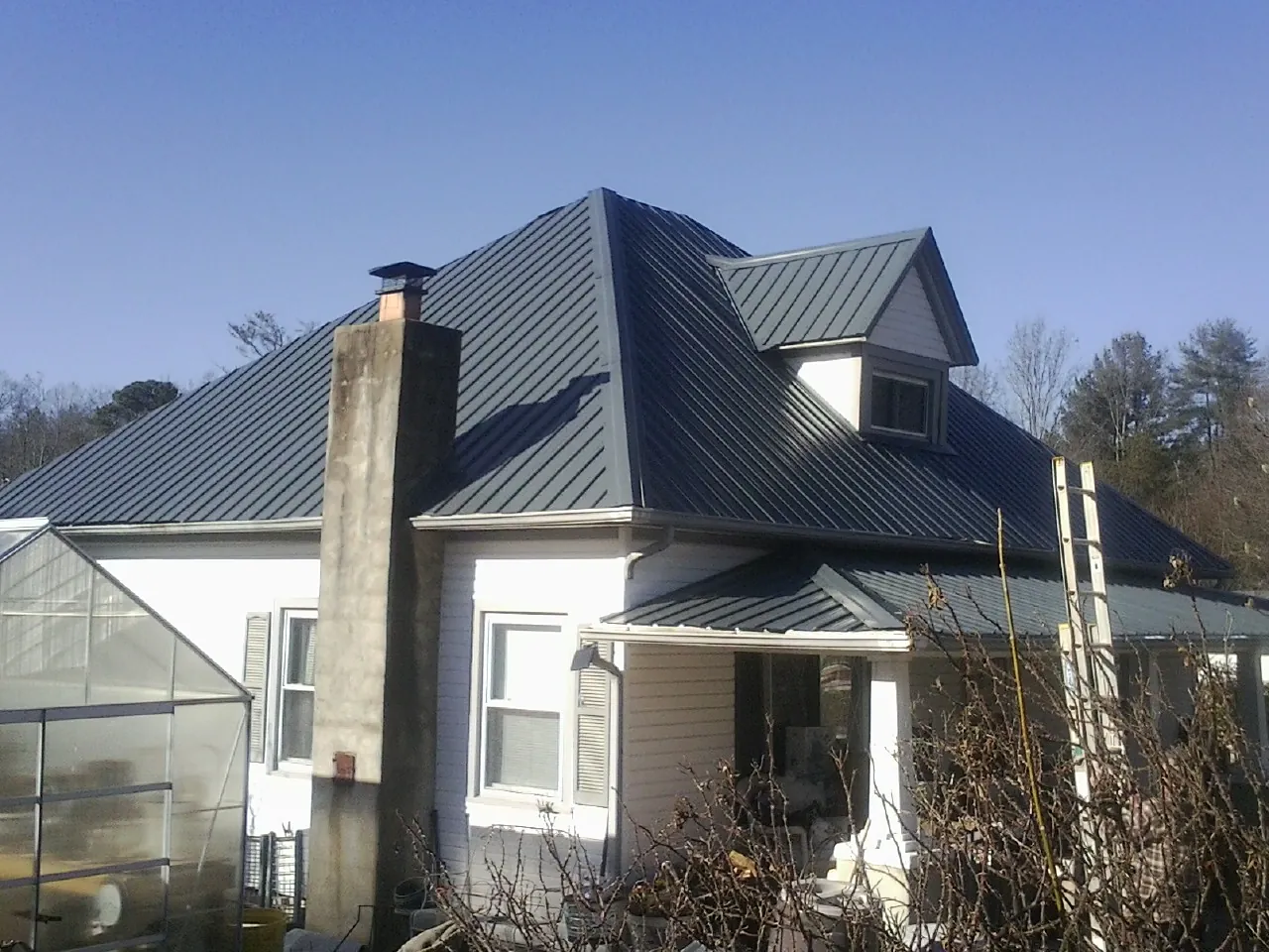 Dark blue standing seam metal roof on a white farmhouse with dormer — Slate & Tile Roof Repair by Roofing Brothers in Tipton