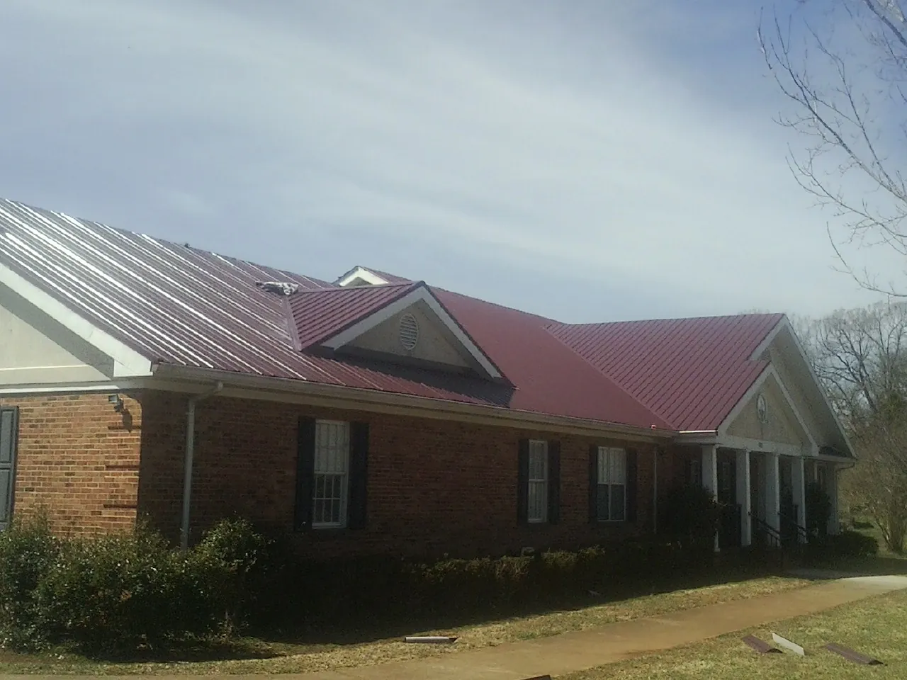 Red metal roof with gabled entries on a long brick building, from a Hail Damage Roof Repair job in Tipton