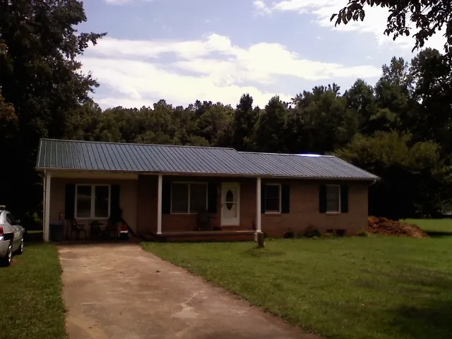 Dark green metal roof on a brick ranch with a covered porch in Tipton